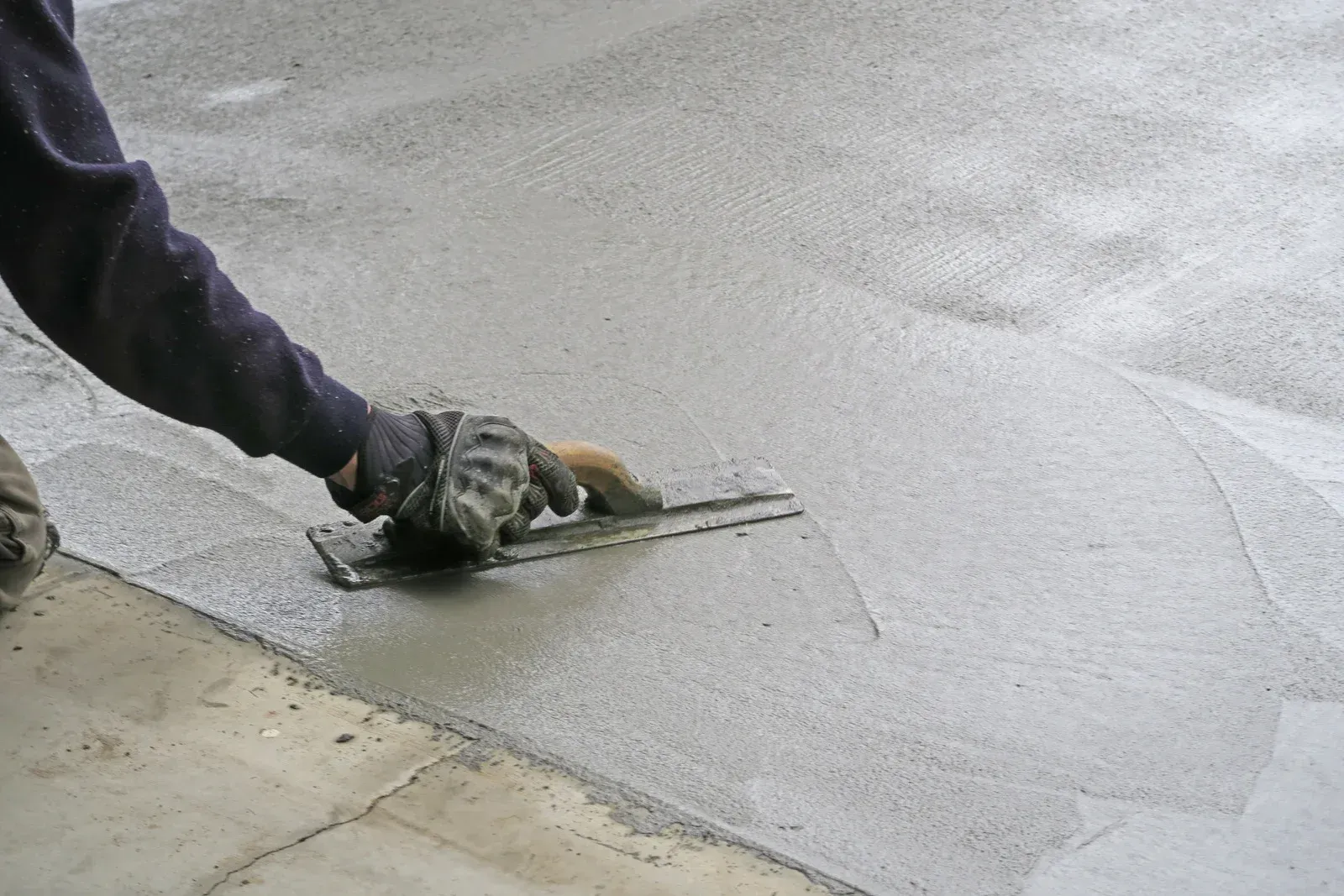A person is using a trowel to spread concrete on a sidewalk.