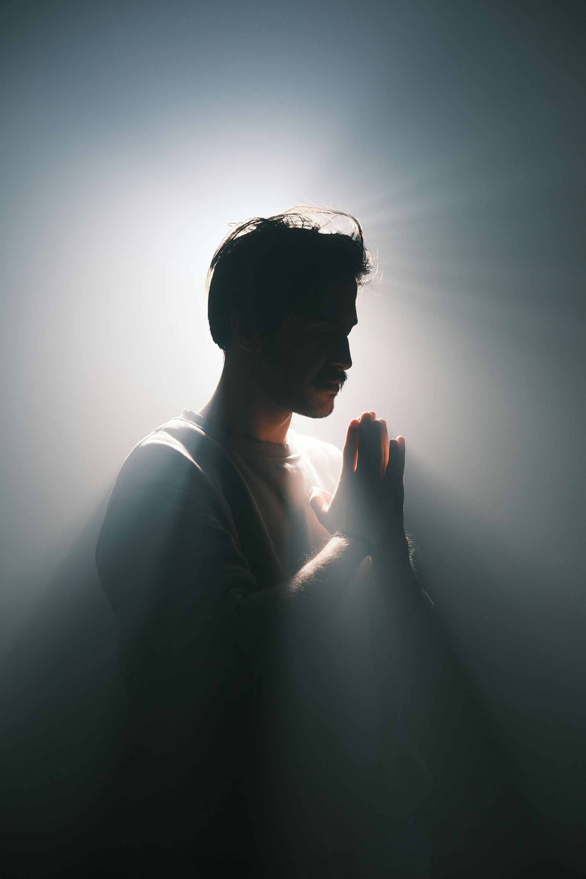 A Man is Praying With His Hands Folded in a Dark Room — Angel of Light Nick Turner In Ballina, NSW