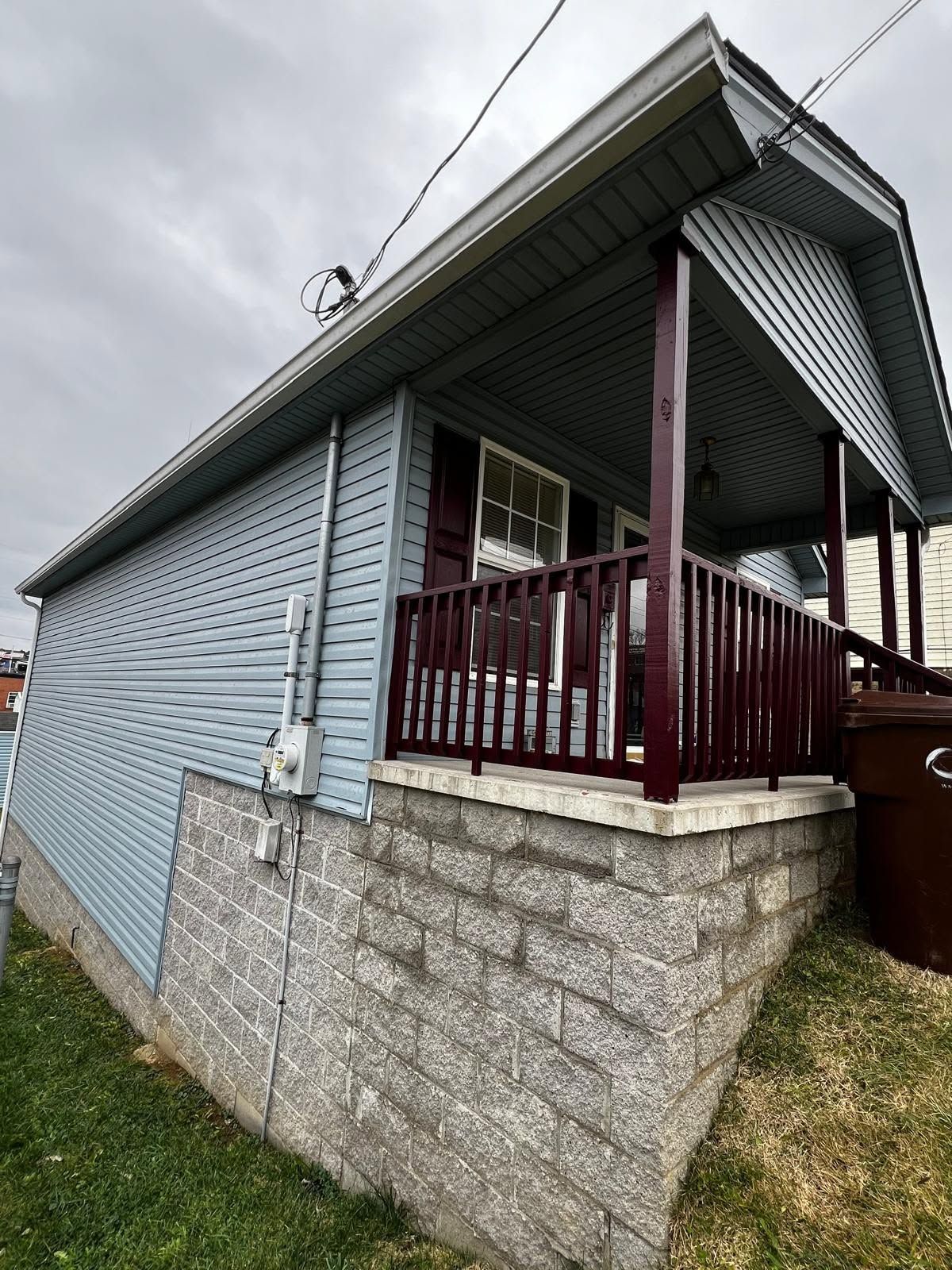 Blue house with maroon porch on a stone foundation, viewed from the side under a cloudy sky