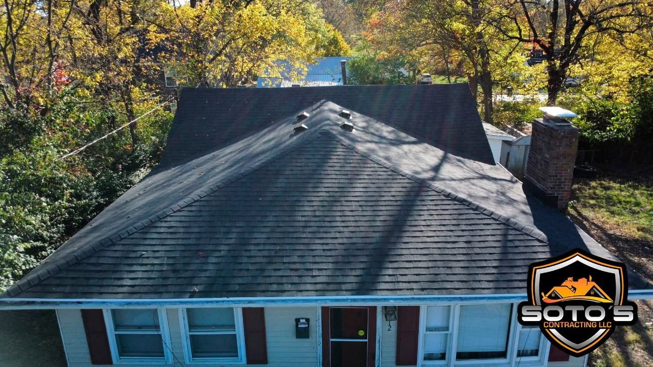 Aerial view of a house with a dark roof and blue siding, surrounded by autumn trees.