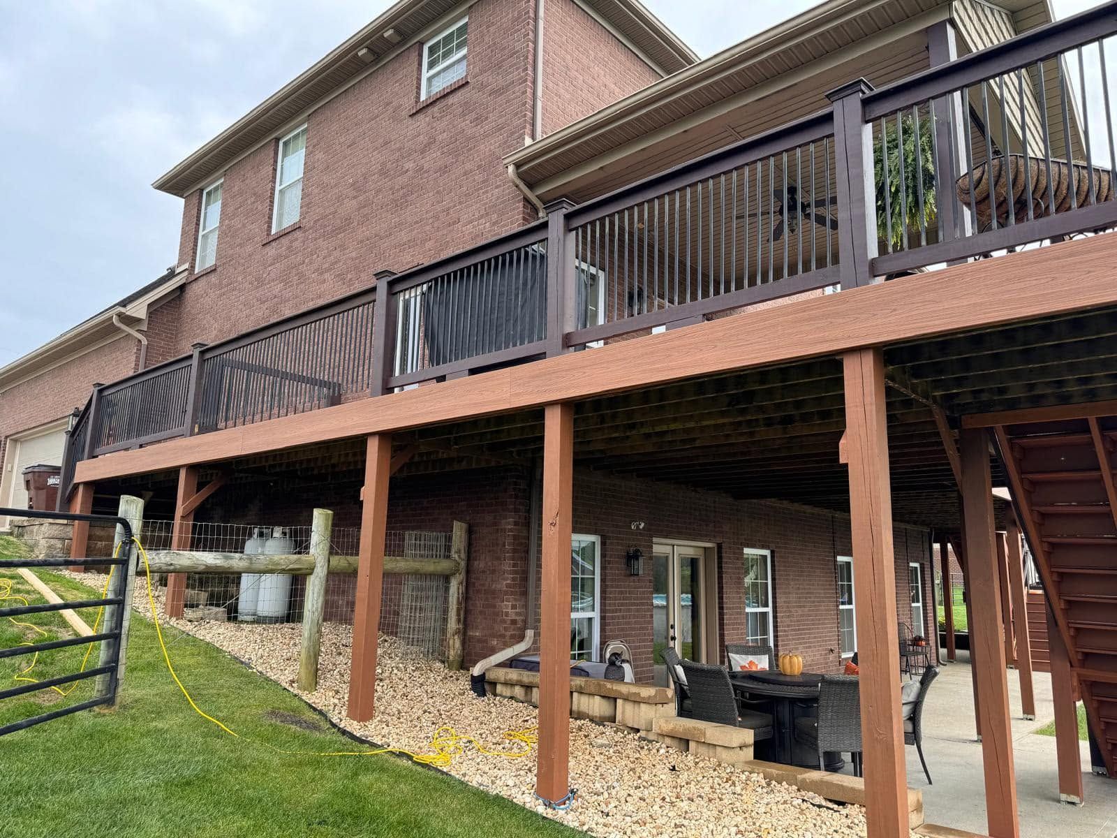 Brick house with raised wooden deck, stairs, and covered patio on a grassy yard