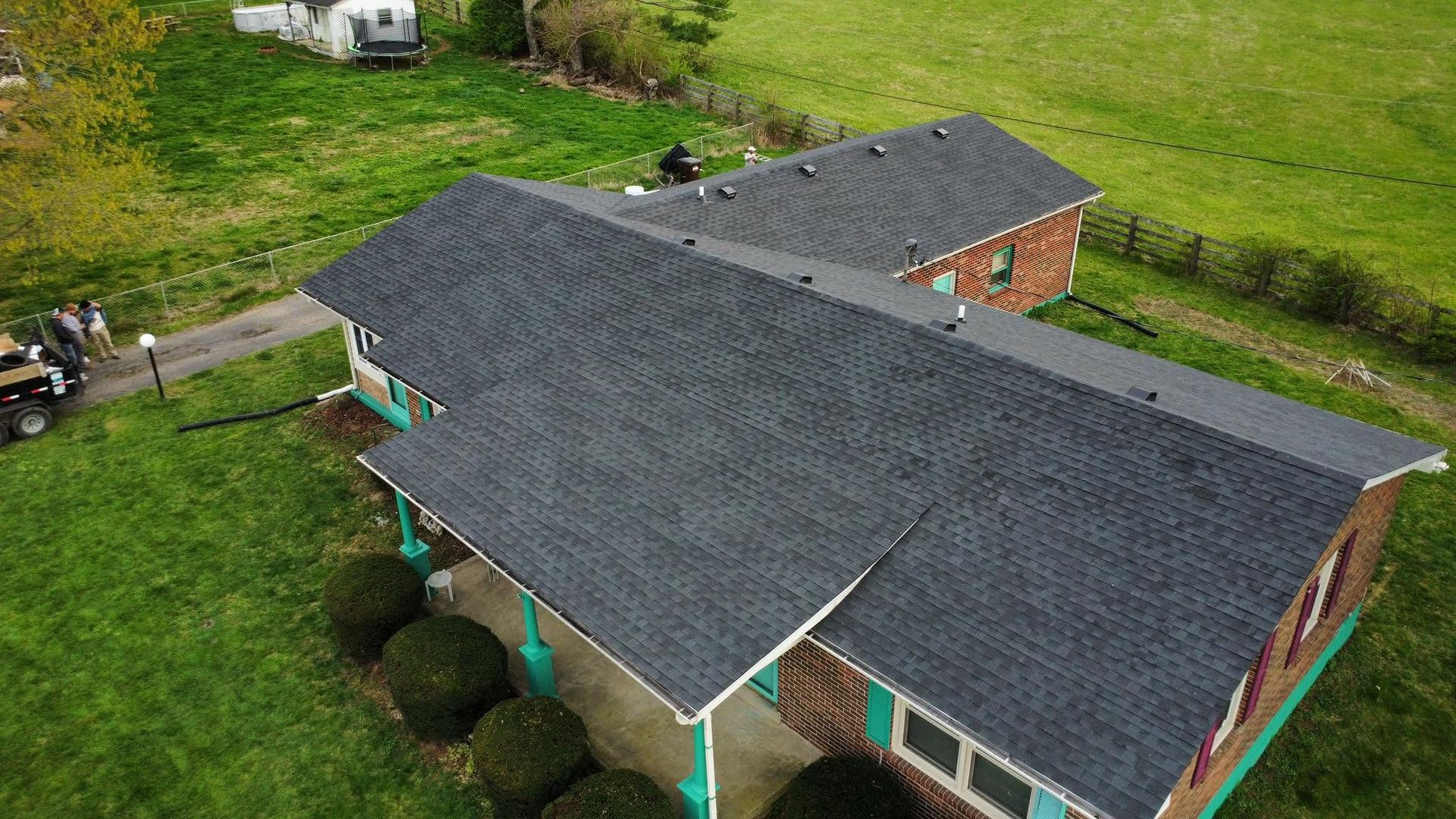 Aerial view of a house with a dark gray roof and green lawn in a rural area.