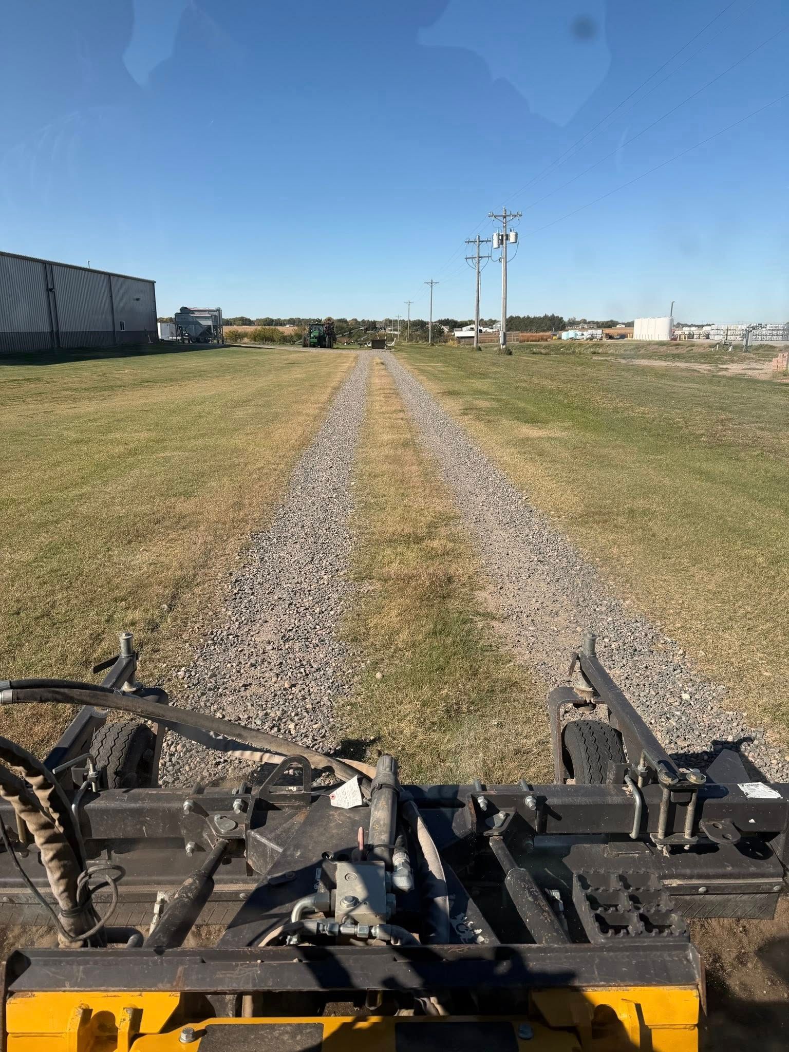 A machine laying gravel for a path through a grassy field on a sunny day.