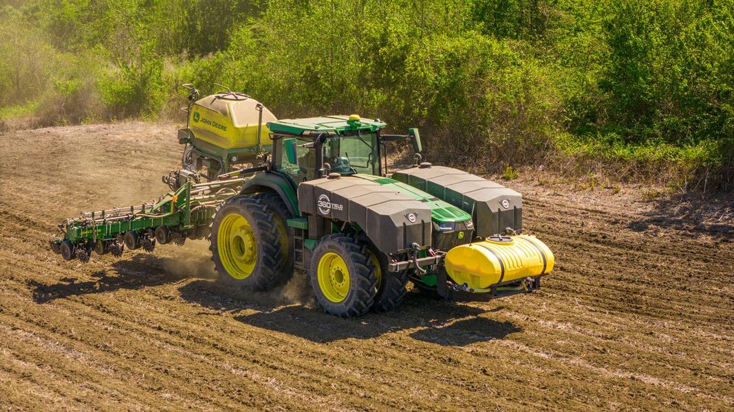 Green and yellow tractor planting seeds in a field.