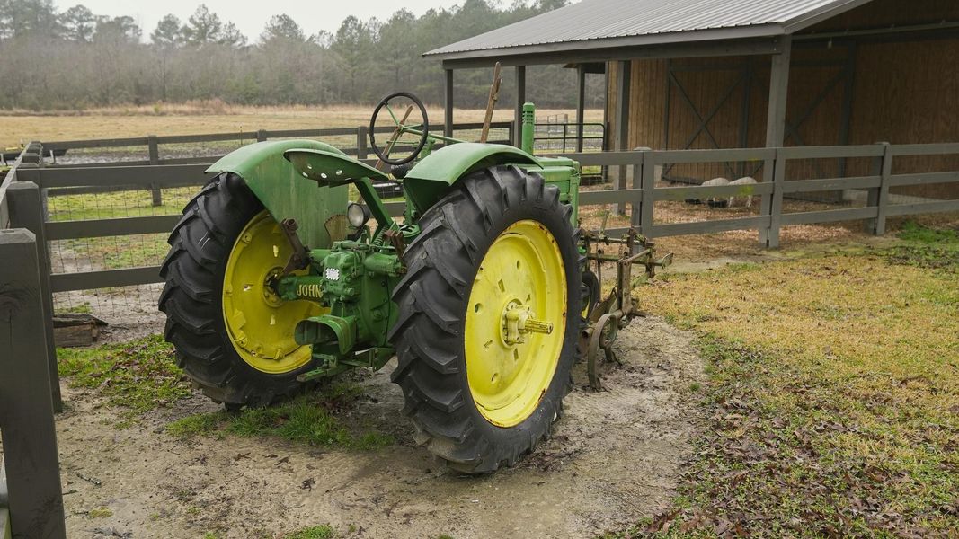 Green and yellow John Deere tractor parked near a wooden fence and barn.