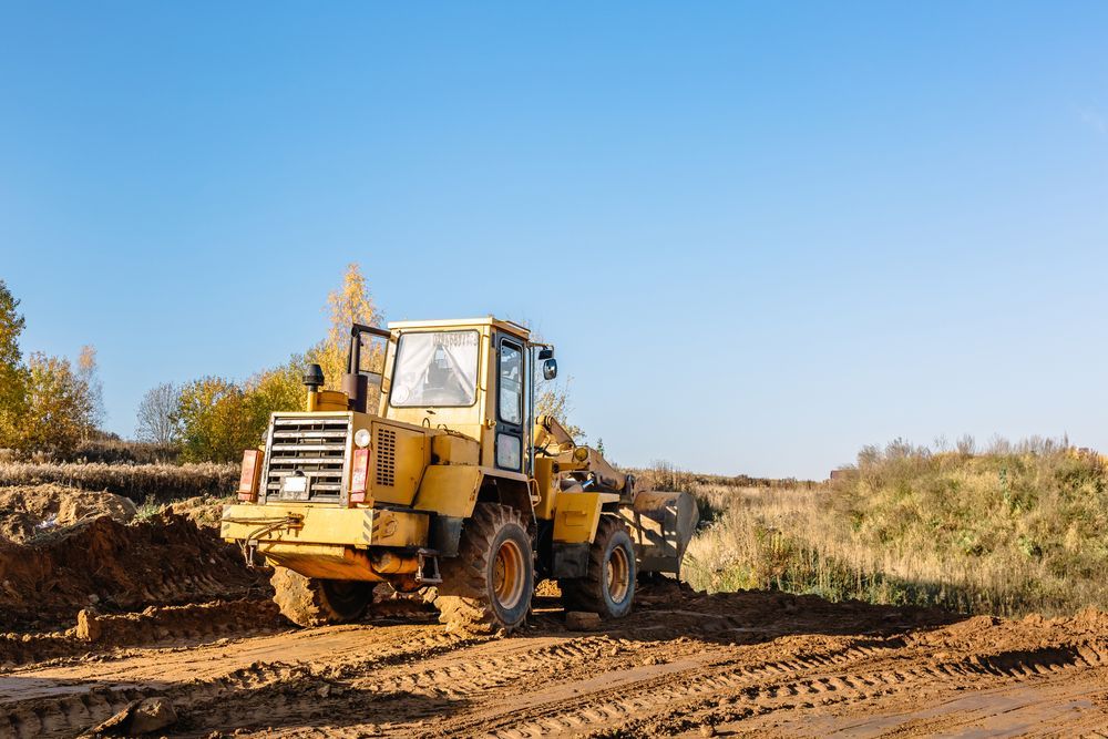 Yellow construction loader on muddy ground under a blue sky.