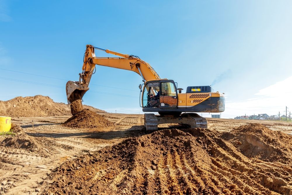 Yellow excavator digging dirt on a construction site under a blue sky.