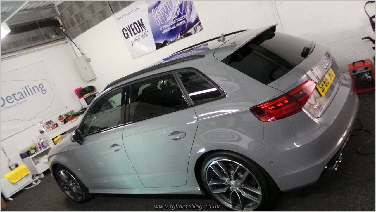 A silver car is parked in a garage next to a sign that says detailing