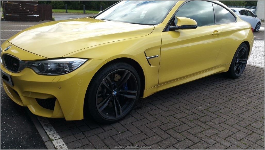 A yellow bmw is parked on a brick driveway