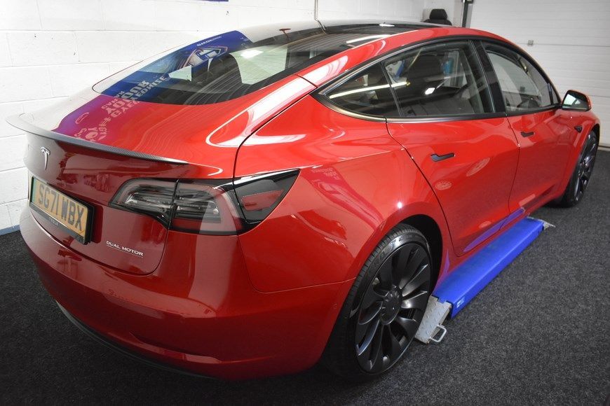 A red tesla model 3 is parked in a garage.