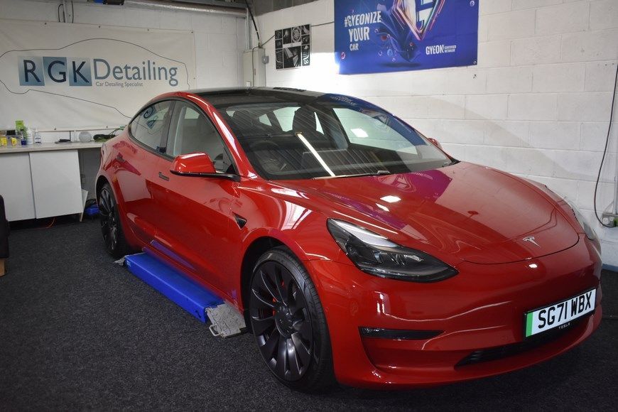 A red tesla model 3 is sitting on a lift in a garage.