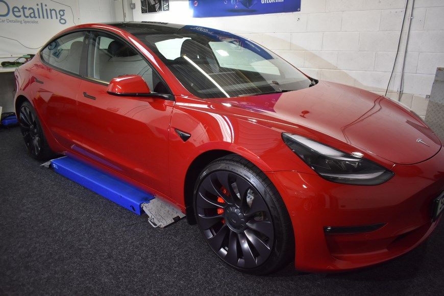 A red tesla model 3 is sitting on a lift in a garage.