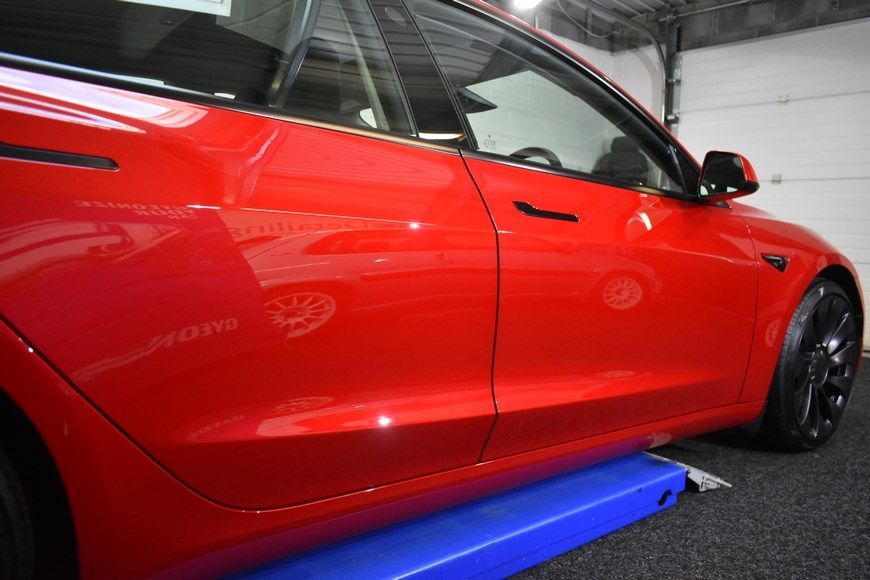 A red tesla model 3 is sitting on a blue ramp in a garage.