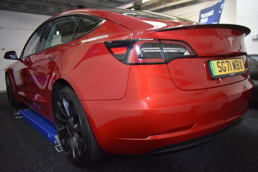 A red tesla model 3 is parked in a garage.