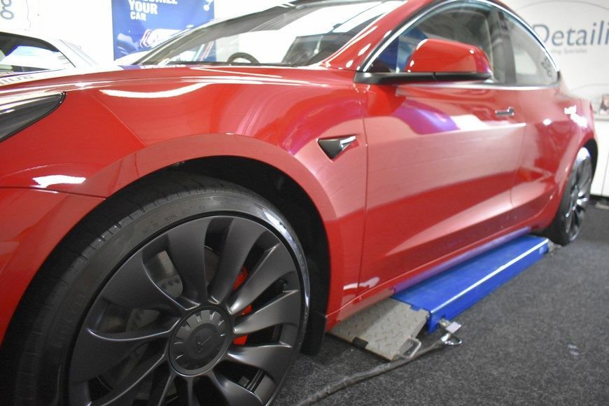 A red tesla model 3 is sitting on a lift