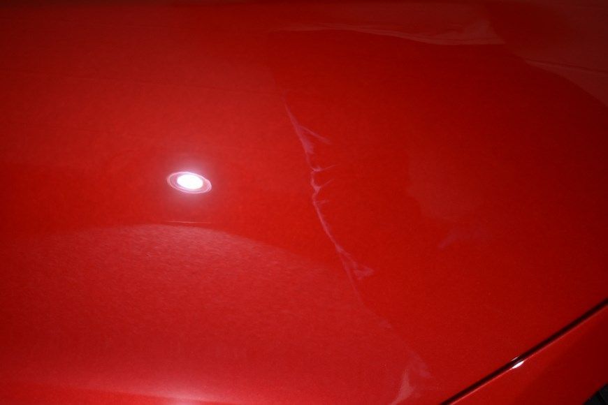 A close up of a red car hood with a light shining on it.