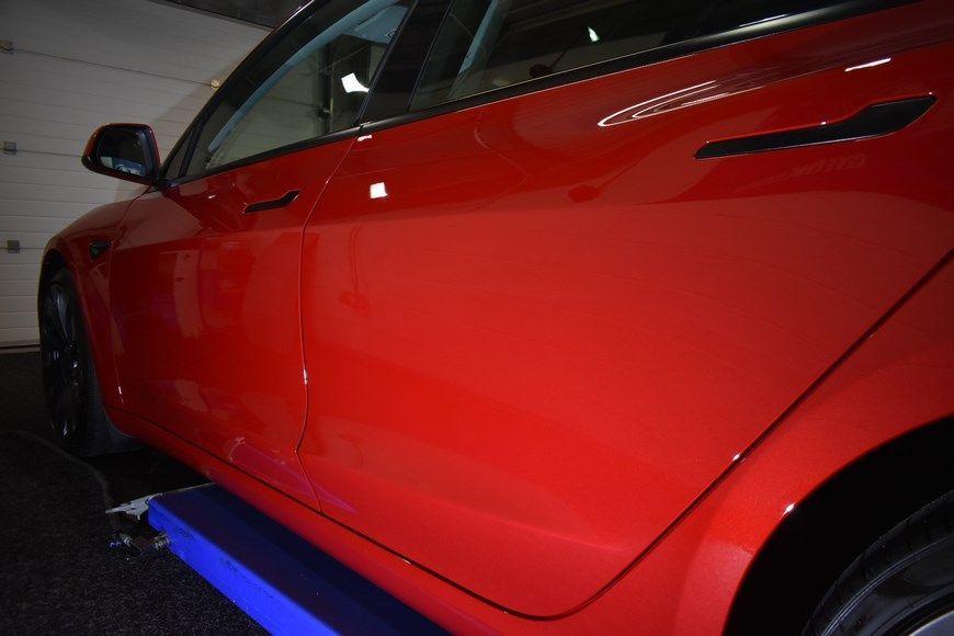 A red tesla model 3 is parked in a garage.