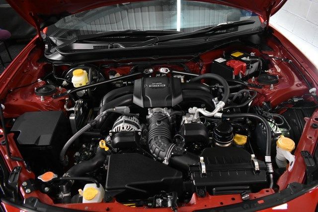 The engine of a red car is shown with the hood open.