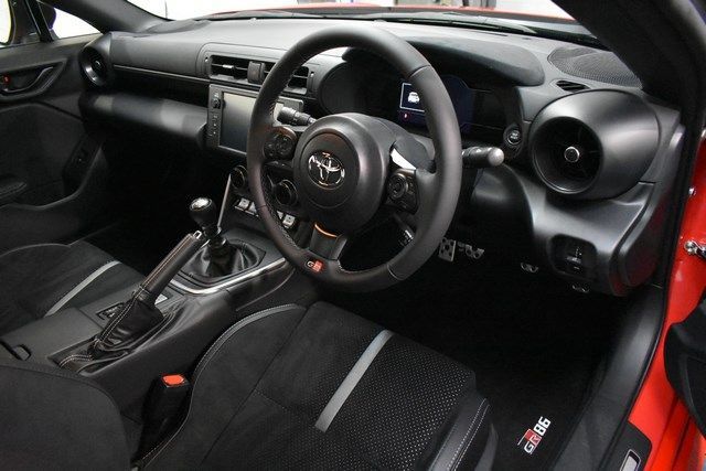 The interior of a red sports car with a black steering wheel.