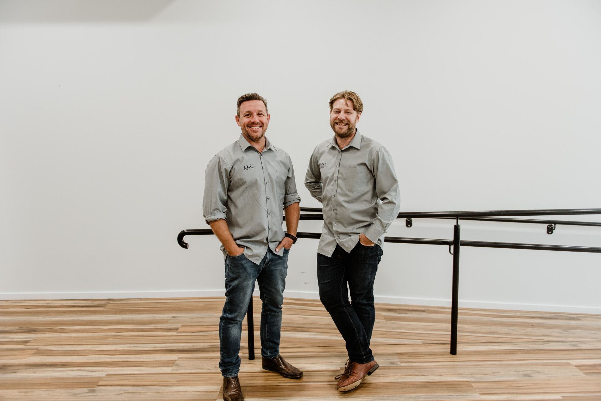 Two Men Smiling, Wearing Casual Shirts and Jeans, Standing Near a Wall — D&C Projects in Tamworth, NSW
