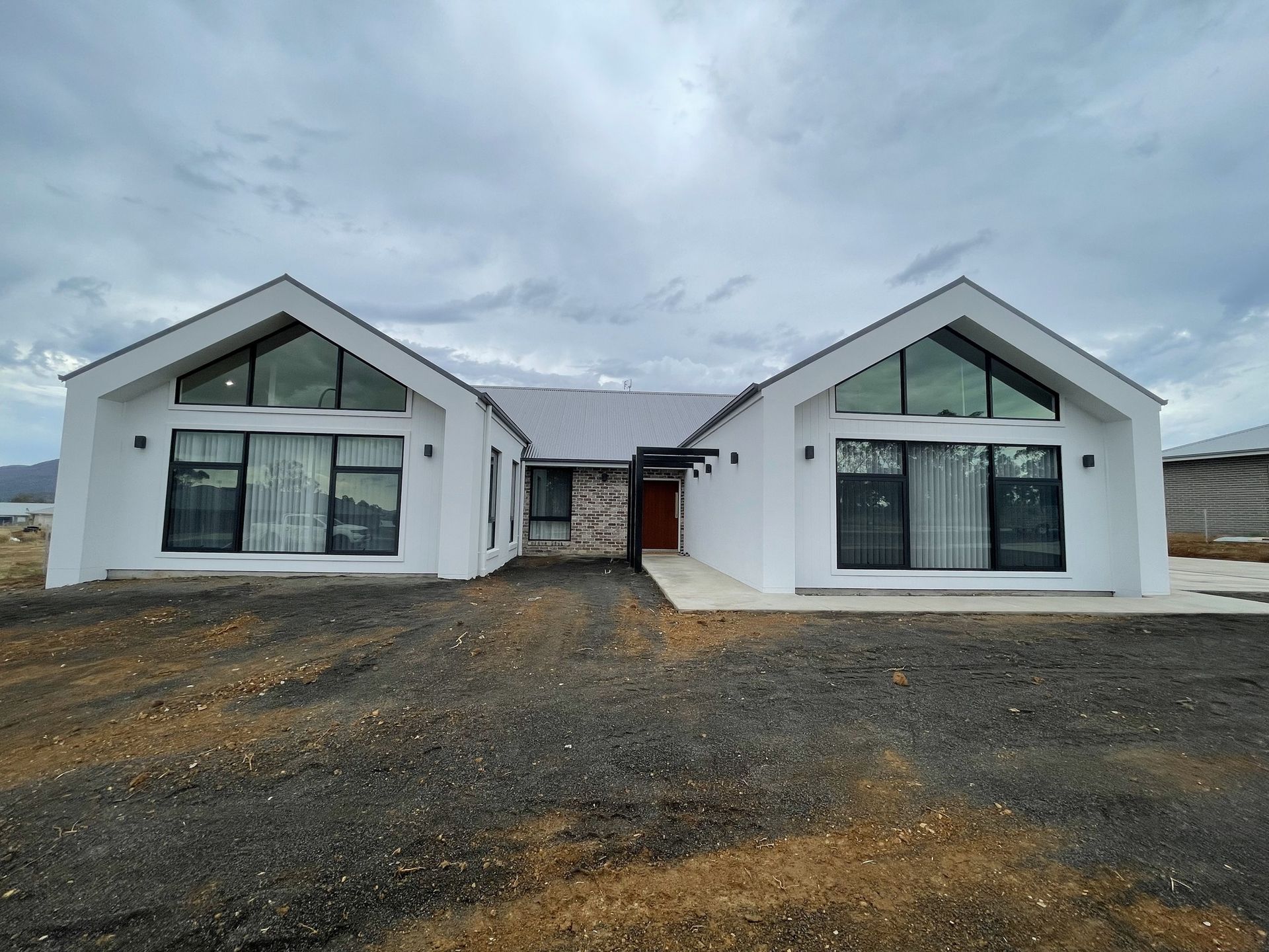 A modern, white, symmetrical house with two gabled wings, large windows, and a central stone entryway under a cloudy sky.