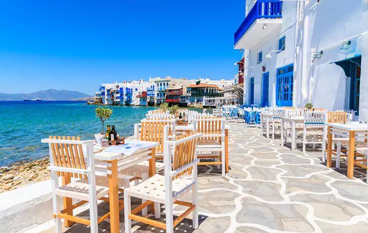 A restaurant with tables and chairs next to the ocean.