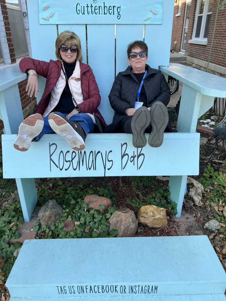 two women are sitting on a blue bench with their feet on it .