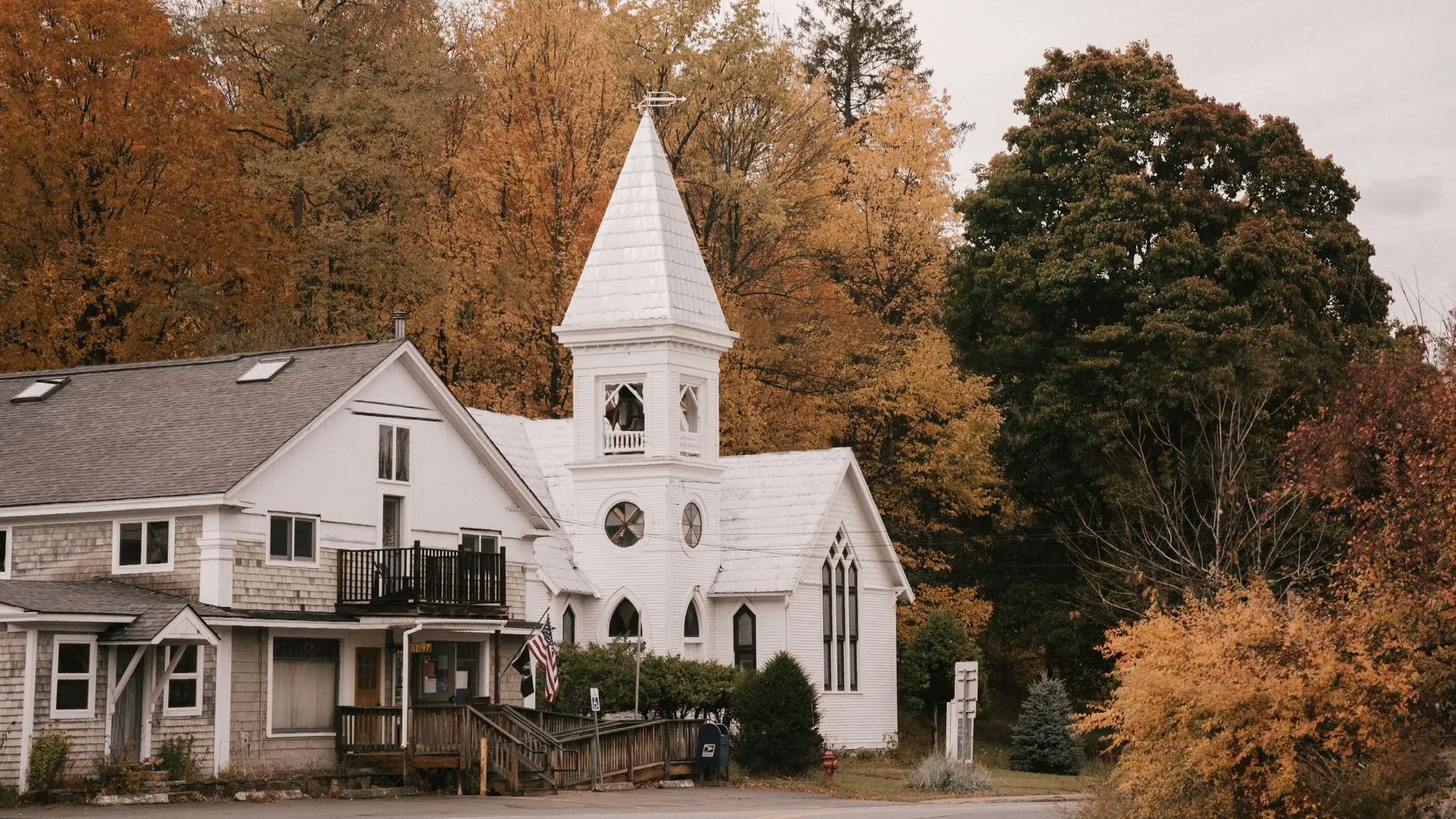a white church with a steeple is surrounded by trees and houses .