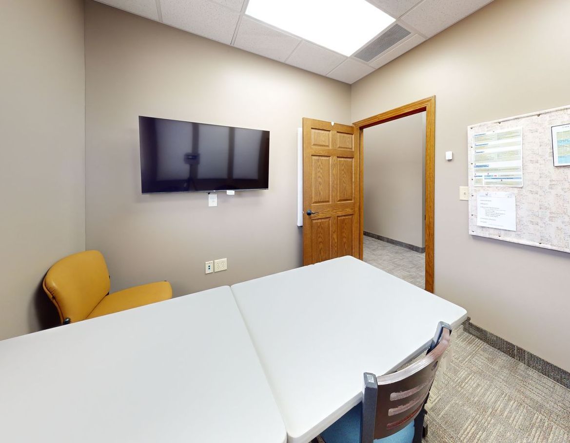 A small conference room with a table and chairs and a flat screen tv on the wall.