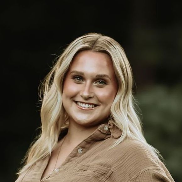 A woman with blonde hair is wearing a black shirt and smiling.