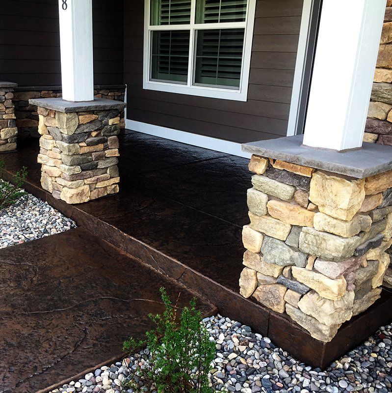 A porch with stone pillars and a concrete walkway