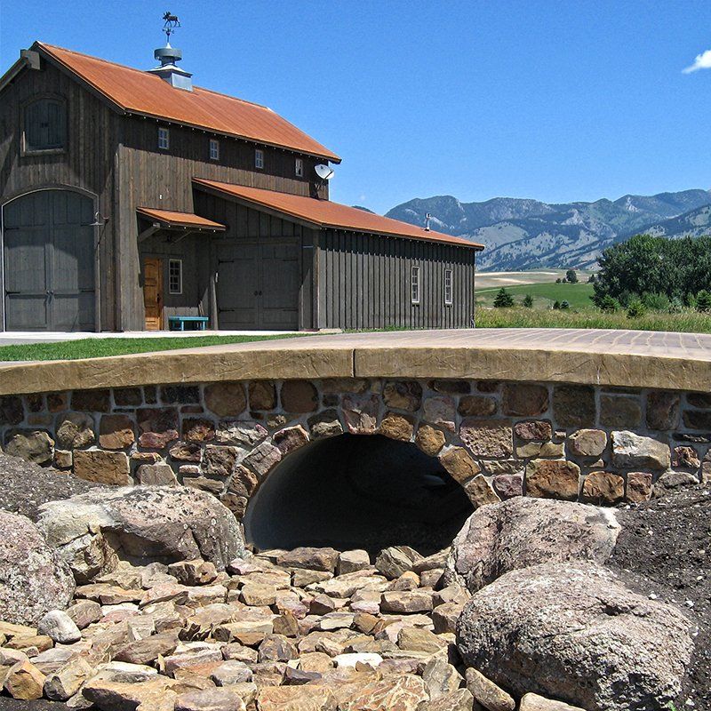 A stone bridge leading to a barn with mountains in the background