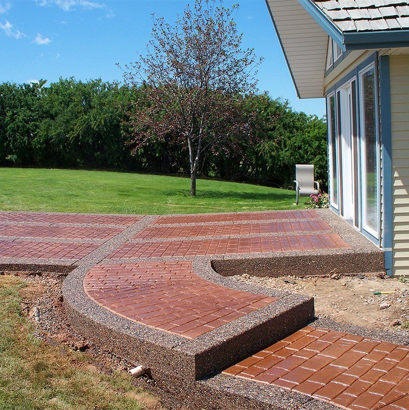A brick walkway leading to a house with a tree in the background