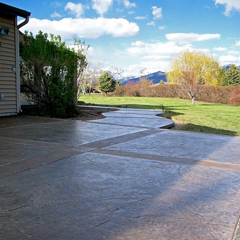 A concrete walkway leading to a grassy field with mountains in the background