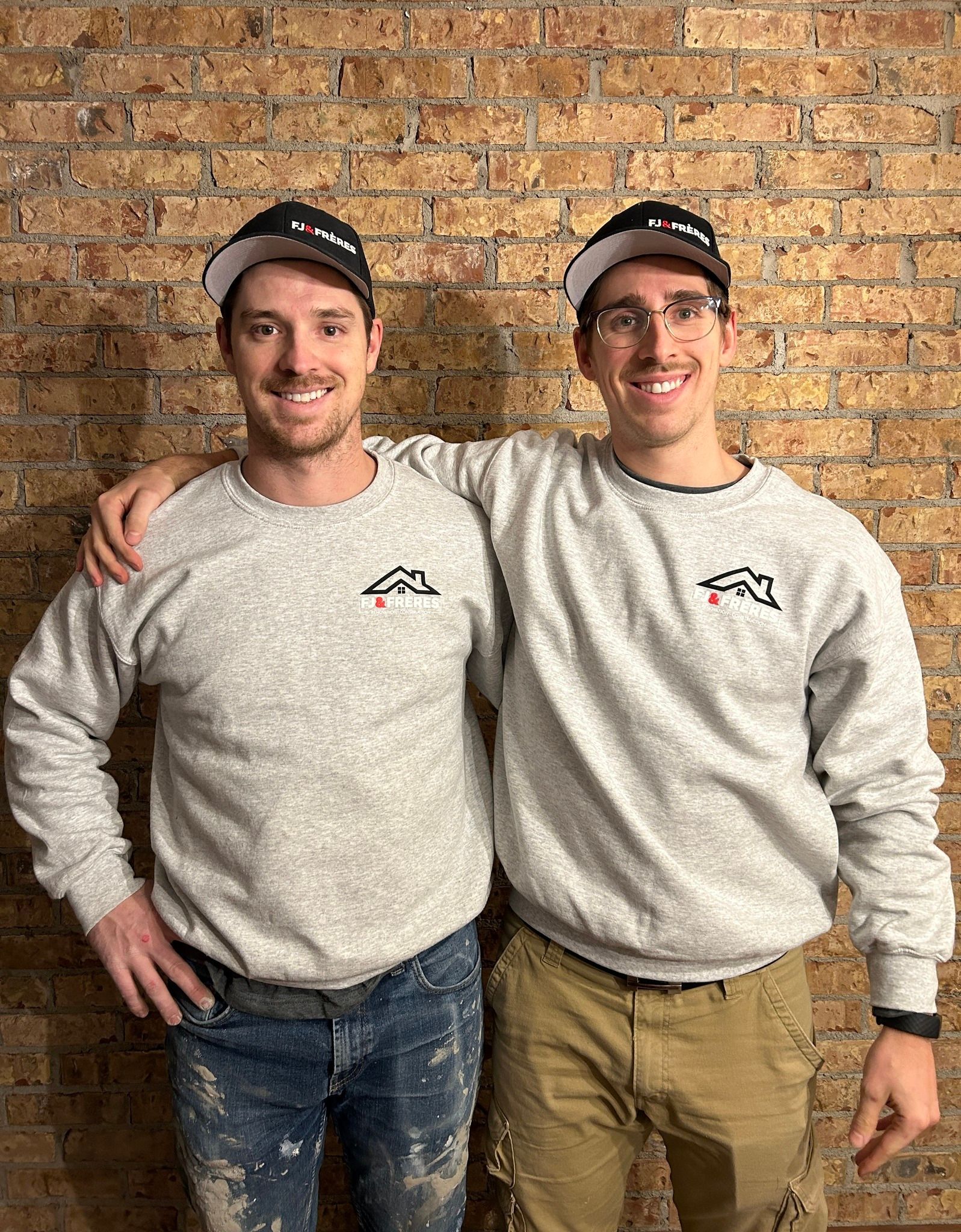 Deux hommes se tiennent côte à côte devant un mur de briques.