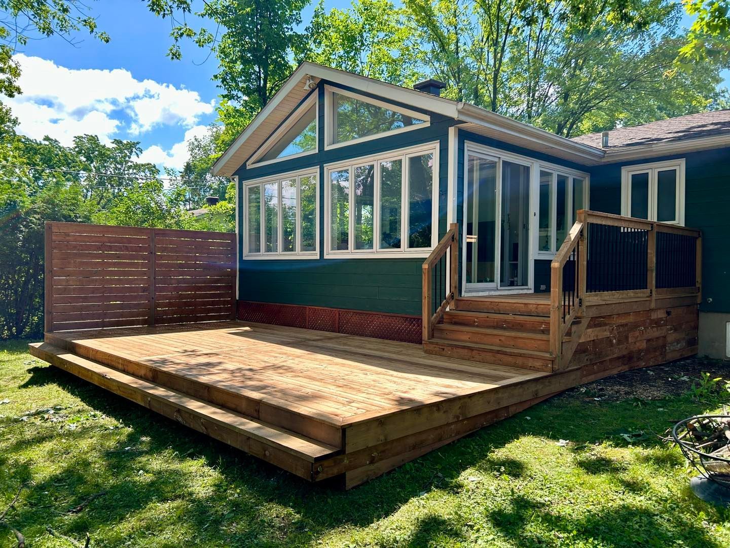 Une maison verte avec une grande terrasse en bois devant elle.
