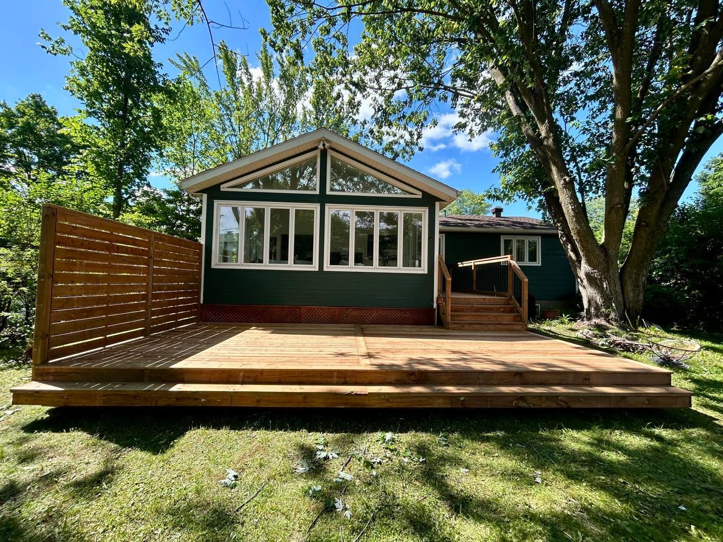 Une maison verte avec une terrasse en bois devant.