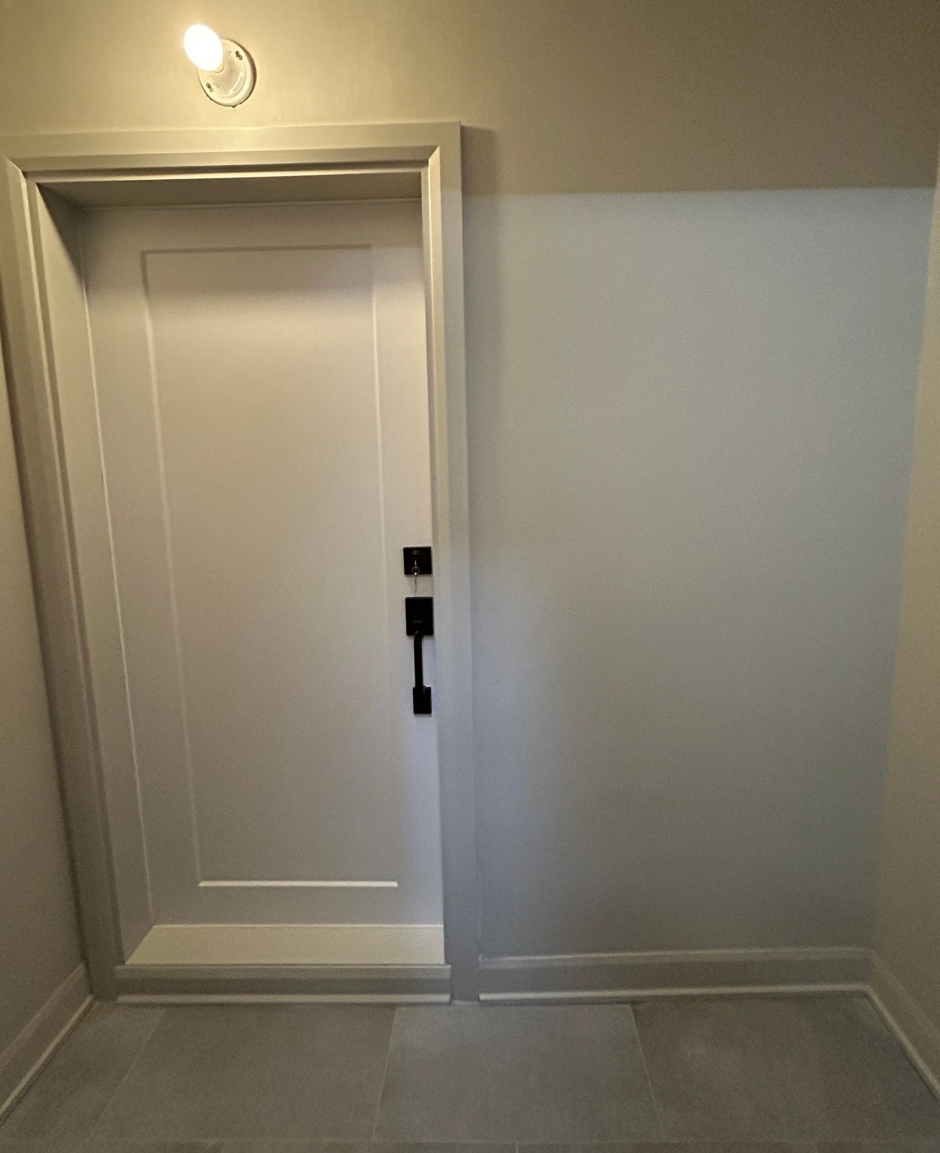 Une porte blanche avec une poignée noire se trouve dans un couloir.