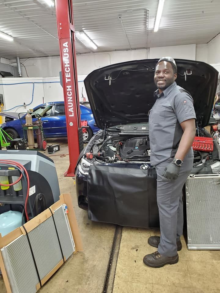 A man is standing in front of a car with the hood up in a garage.