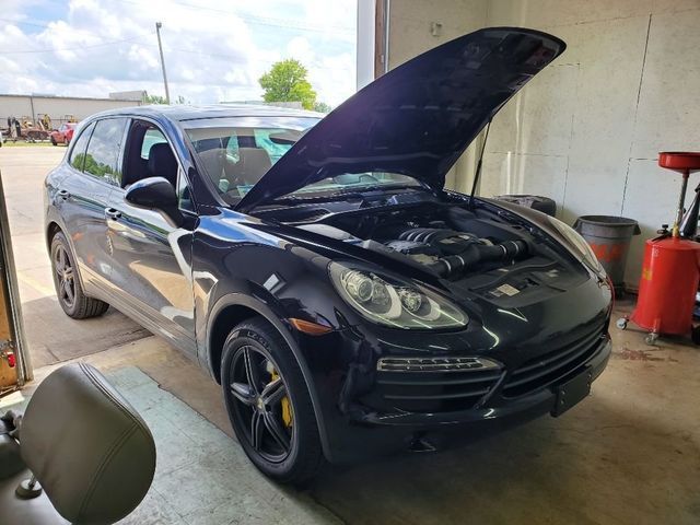A black porsche cayenne with the hood up is parked in a garage.