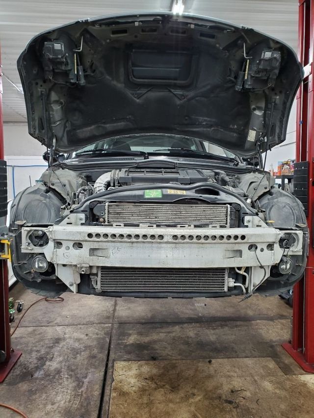 A car with the hood up is on a lift in a garage.
