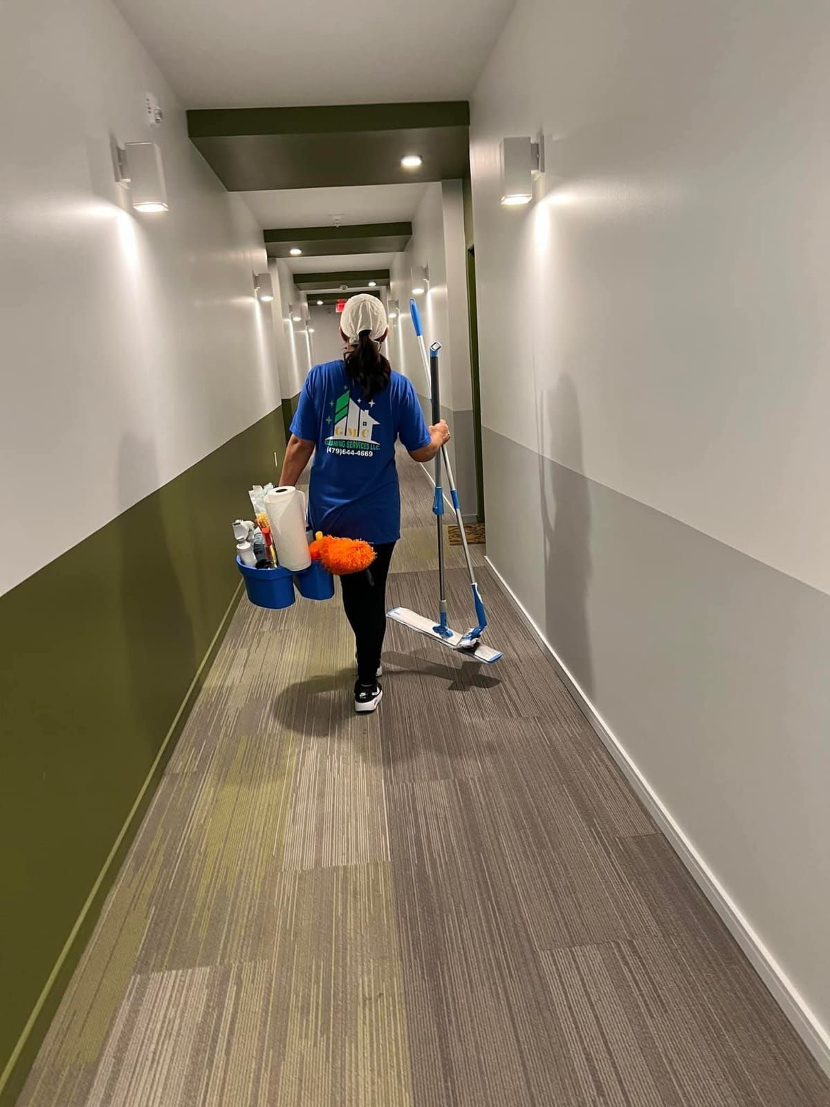 A woman is cleaning a hallway with a mop and bucket.
