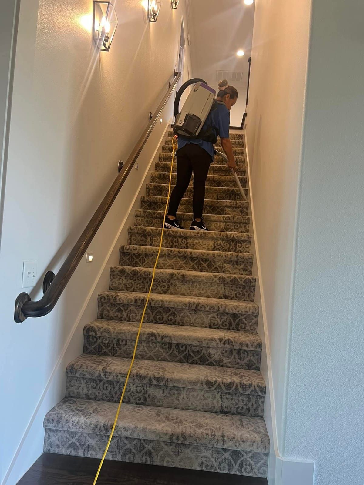 A woman is cleaning the stairs with a vacuum cleaner.
