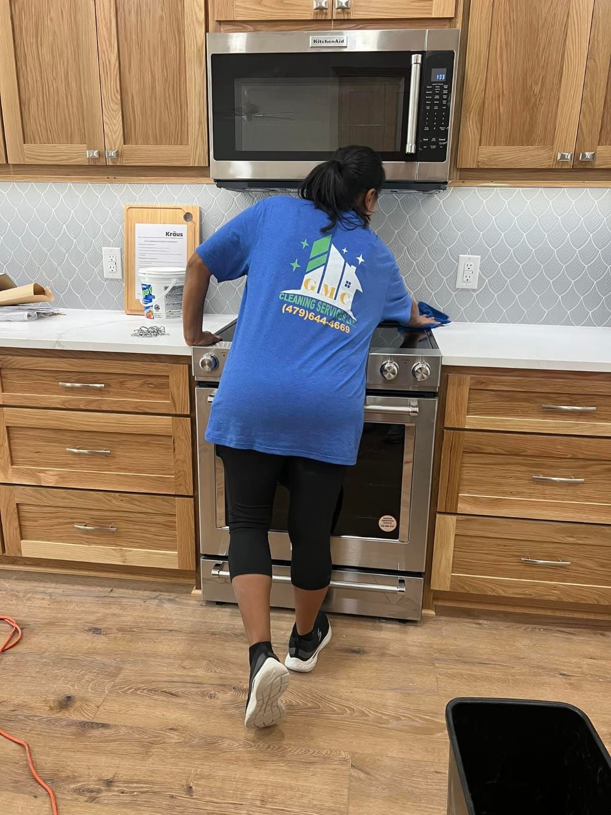 A woman in a blue shirt is cleaning a stove in a kitchen.