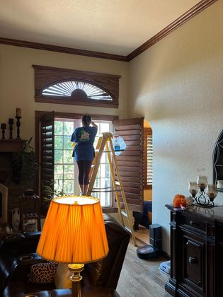 A woman on a ladder cleaning a window in a living room
