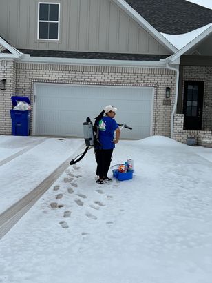 A woman is cleaning the snow from the driveway of a house.