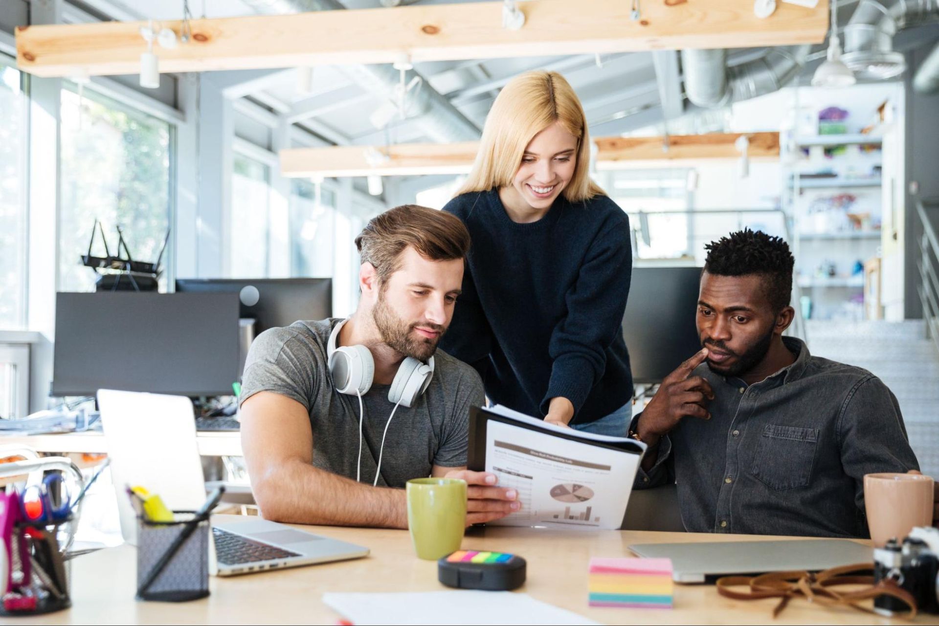 Three coworkers reviewing a printed report together at a desk in a modern office.