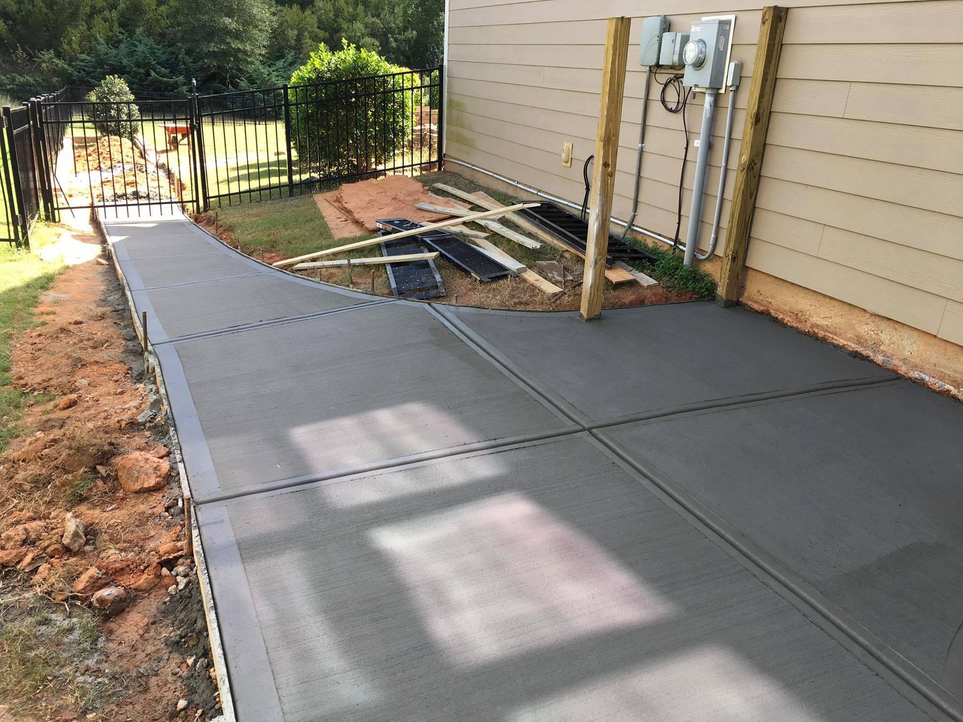 Freshly poured concrete patio and walkway next to a building, with wood framing and electrical fixtures visible.