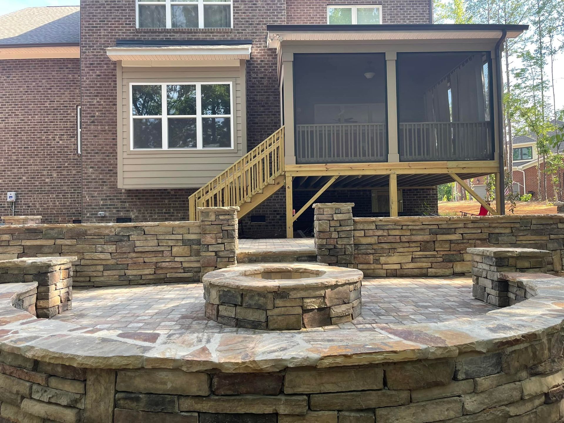 Backyard patio with stone fire pit, seating, steps up to screened porch, and brick house.