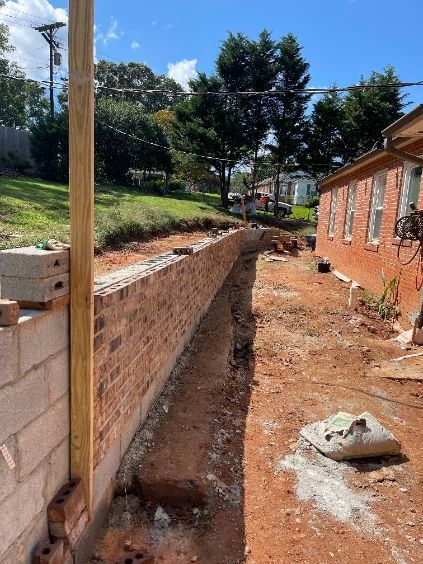 Construction site: Brick retaining wall being built alongside a red-brick building; dirt ground.